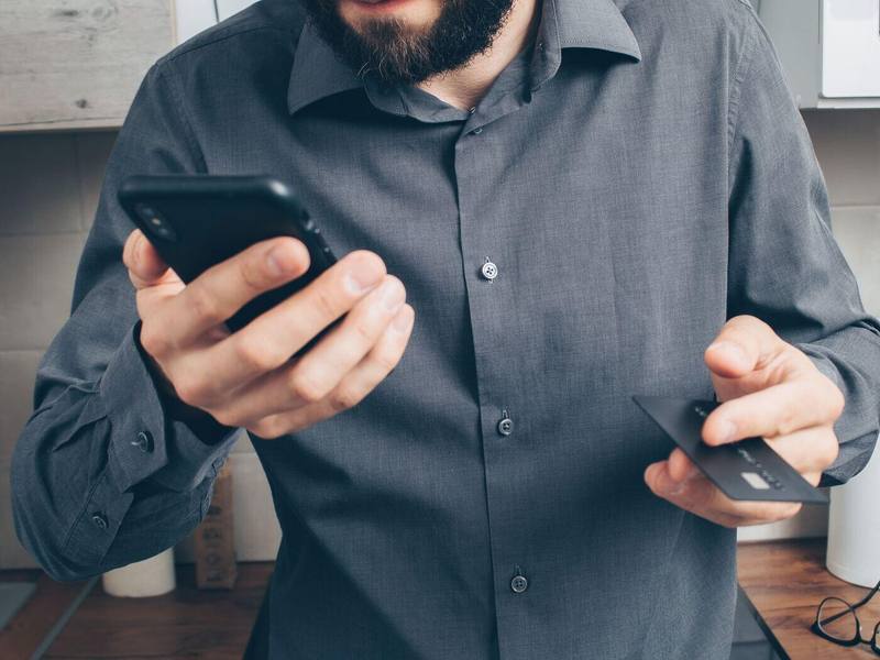 Ein Mann im grauen Hemd hält in der einen Hand sein Telefon und in der anderen eine Karte.