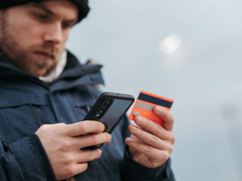 Ein Mann in Winterjacke und Mütze steht draußen und hält sein Telefon an eine Karte.
